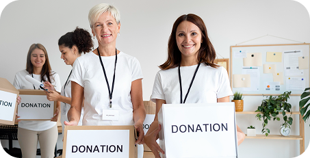 Women volunteers holding donation boxes indoors, smiling and working together to support a community donation drive.