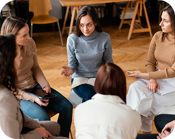 A group of women sitting in a circle, engaged in a conversation, with one woman speaking while others listen attentively.
